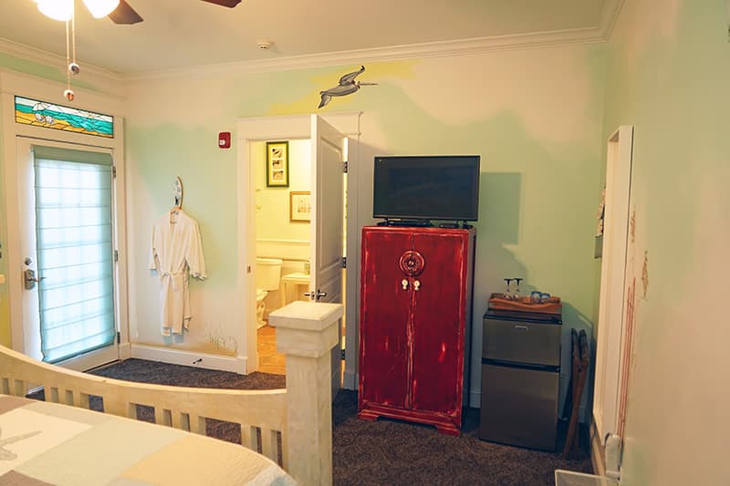 This playful, sea-themed bedroom features light green walls with painted murals, a television atop a red cabinet, and a door leading to a bathroom, with a robe hanging beside the entrance.
