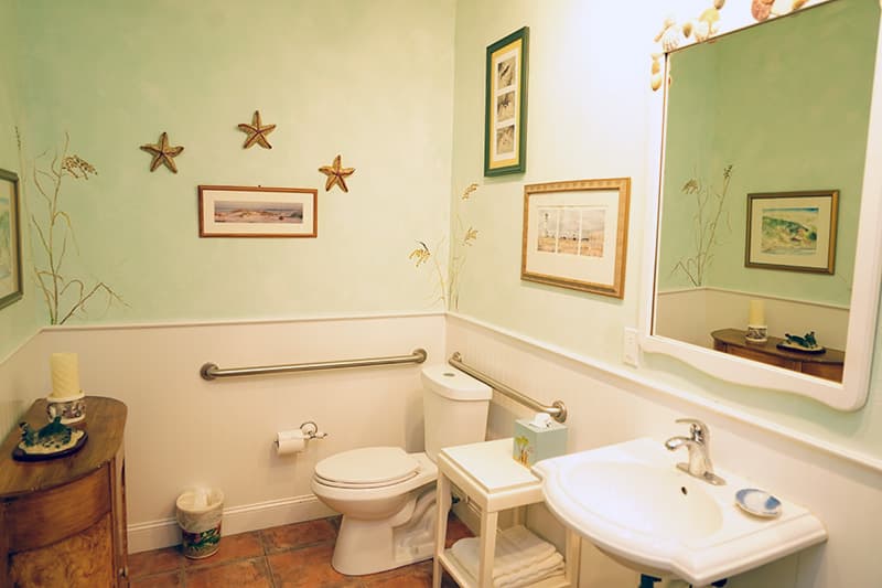 This coastal-themed bathroom features light green walls with starfish decor, a white pedestal sink, a toilet with grab bars, and framed artwork.