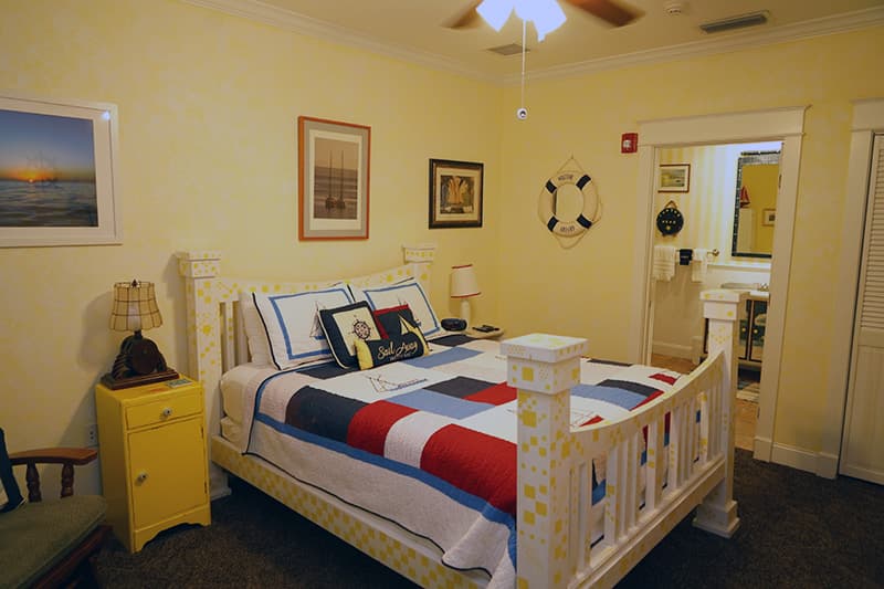 This cheerful bedroom features pale yellow walls, a white wooden bed with nautical bedding and star accents, and a view into a private bathroom.