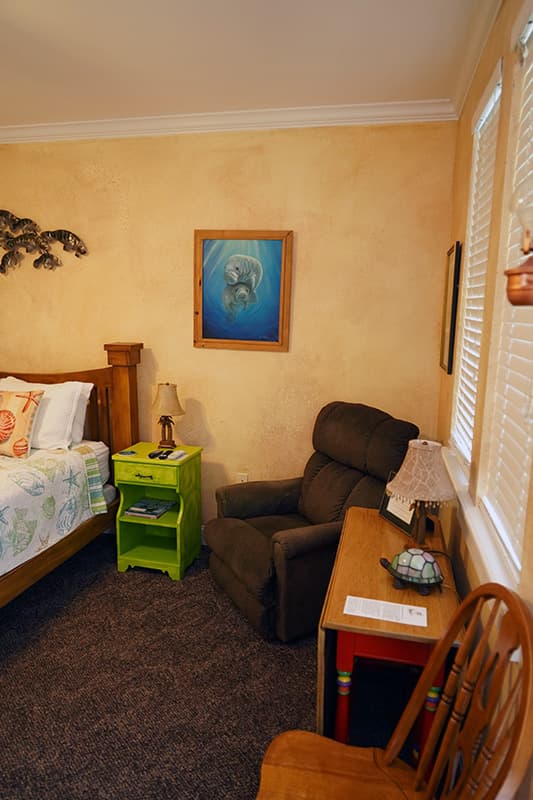 This cozy corner of a bedroom features warm, textured yellow walls, a vibrant green nightstand, a brown recliner, and framed artwork.