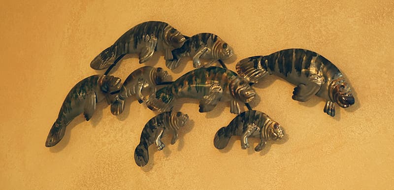 A group of decorative manatee figures, varying in size, are arranged on a warm, textured yellow wall.