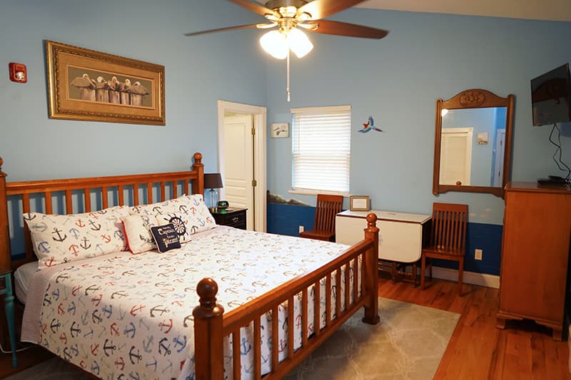 This spacious bedroom features a wooden bed with patterned bedding, light blue walls with a darker blue wainscoting, and a vintage-style mirror, creating a cozy atmosphere.
