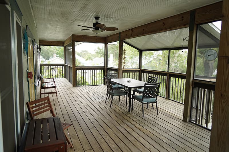 This spacious screened-in porch features wooden decking, a dining table with chairs, and additional seating, offering a comfortable outdoor living area.