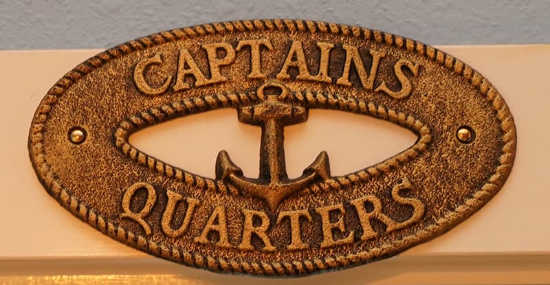 A weathered bronze oval plaque reads "CAPTAINS QUARTERS" with an anchor design in the center, framed by a rope-like border.