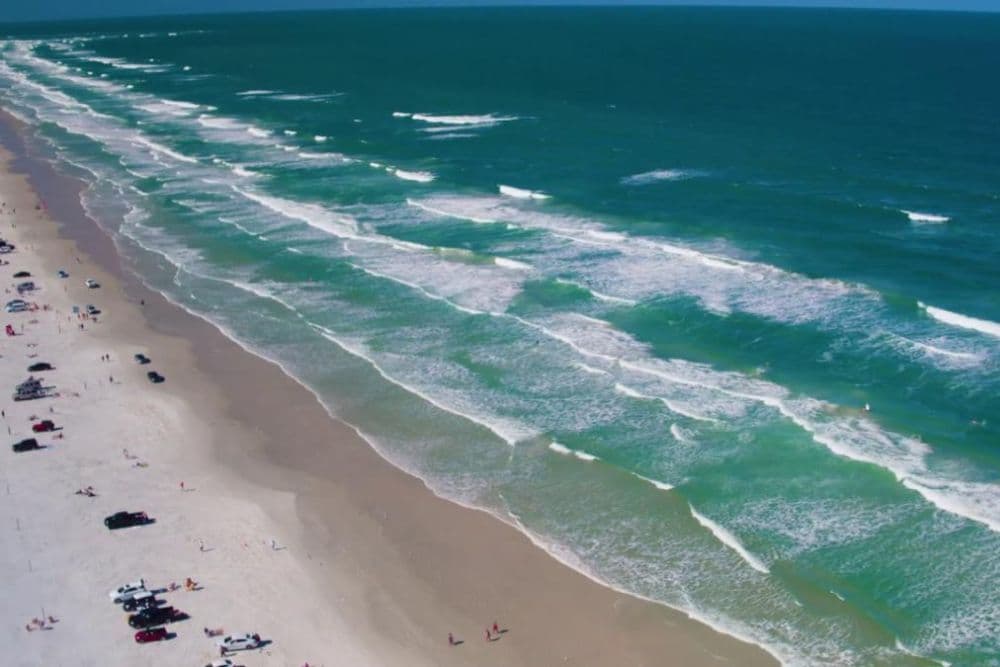 Aerial view of a sandy beach with gentle waves and scattered beachgoers.