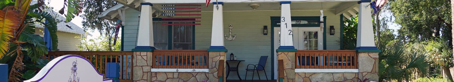 Front view of a charming house with a porch and tropical plants.