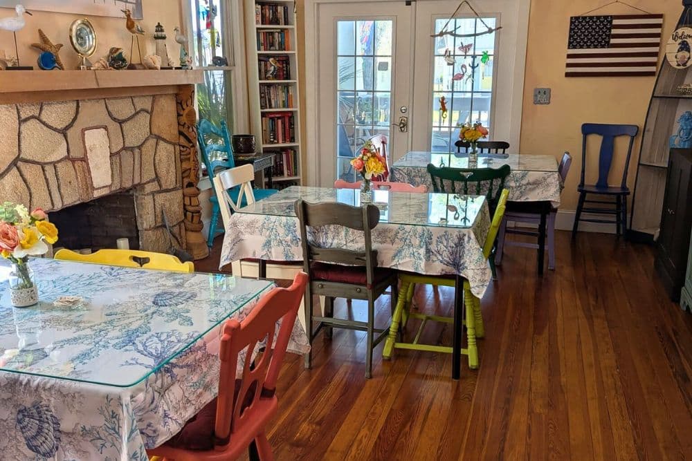 A cozy dining area features colorful tables with floral tablecloths and a stone fireplace.