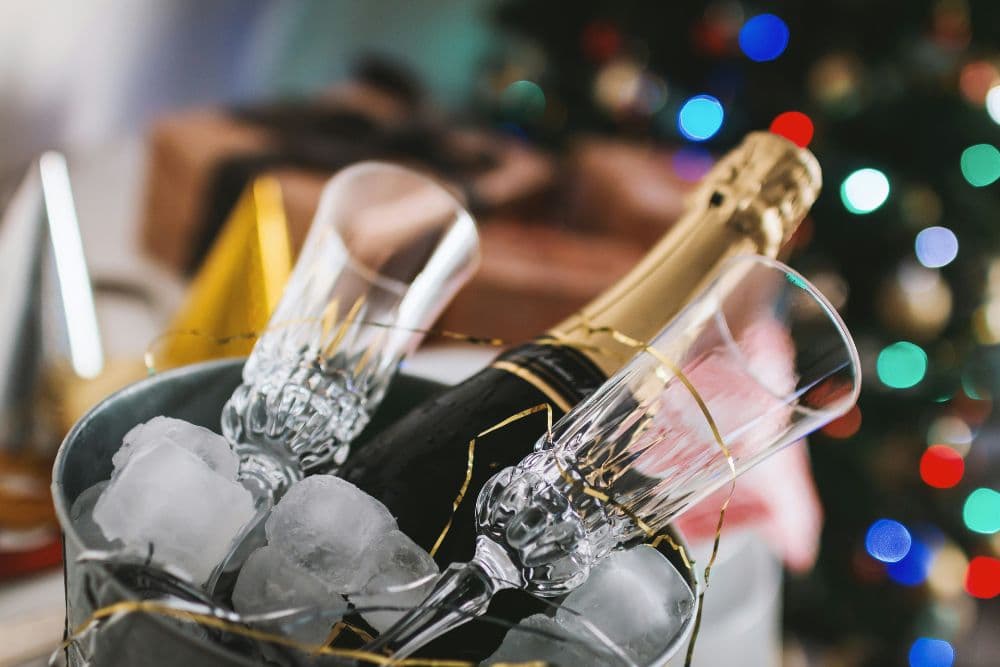 A bottle of champagne nestled in ice with two fluted glasses nearby, against a festive backdrop.