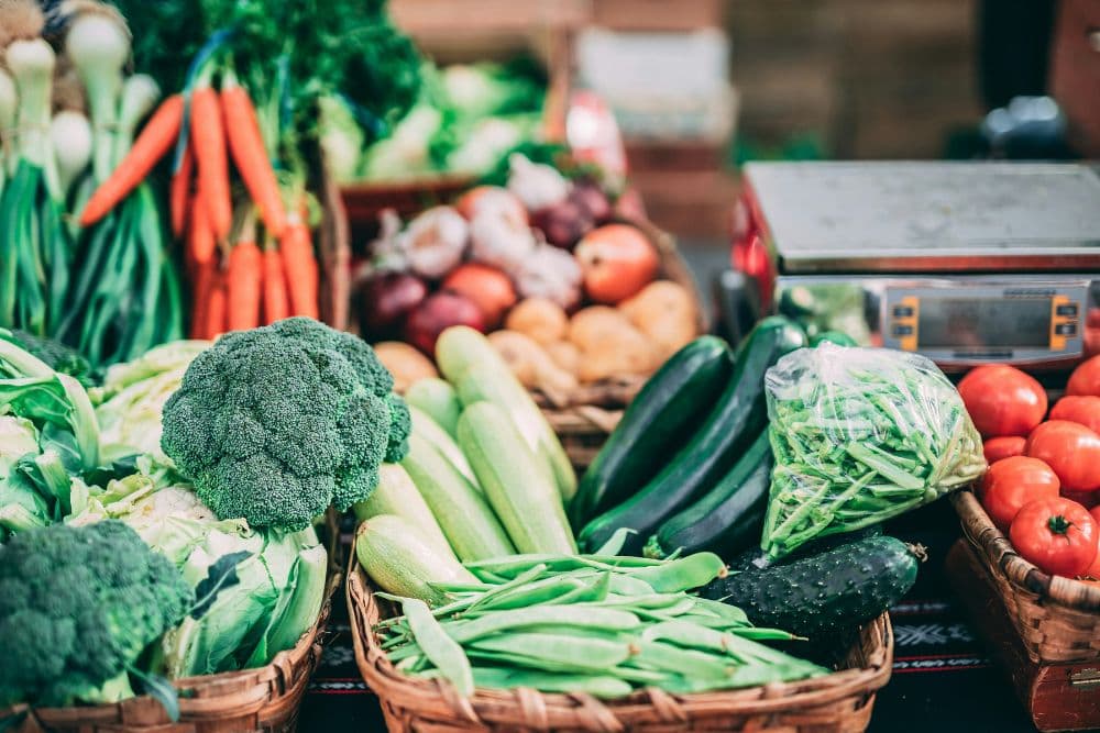 A variety of fresh vegetables including broccoli, carrots, zucchini, and tomatoes displayed in baskets at a market.
