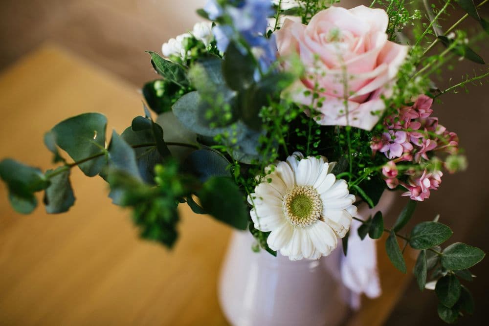 A bouquet of assorted flowers including pink roses, white daisies, and greenery in a vase.