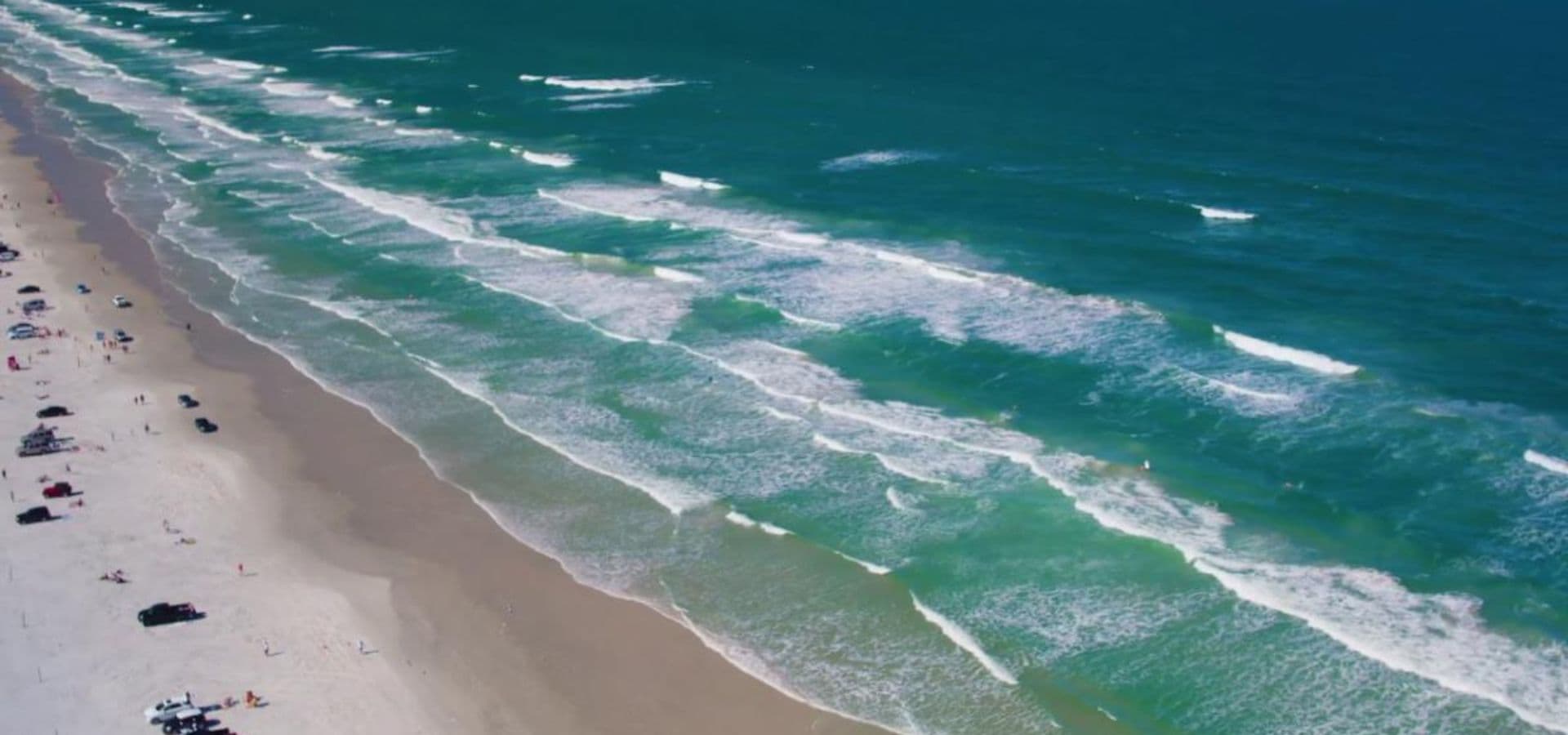 Expansive beach with teal blue waters, whitecaps and people on the beach Expansive beach with teal blue waters, whitecaps and people on the beach