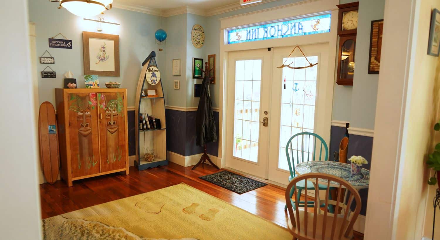 Front foyer of a home with stained glass window, hardwood floors, decorative rug, table with two chairs, seashore decor