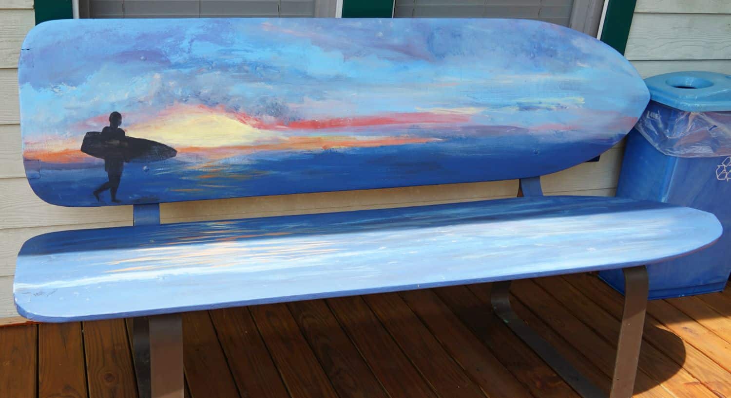 Seating bench in the shape of surfboards, painted blue with a silhouette of a surfer holding a surfboard