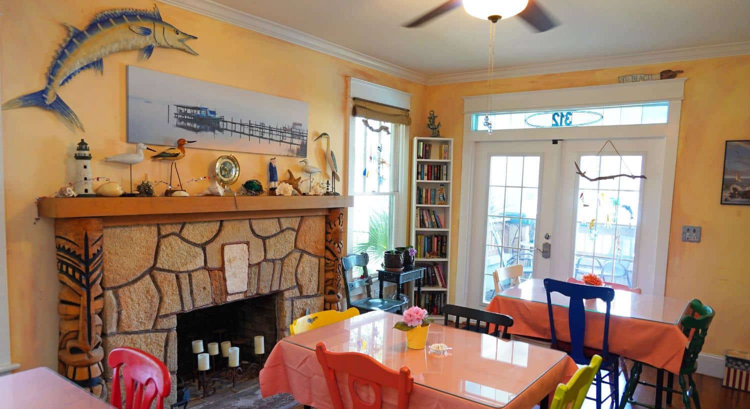 Bright dining room with yellow walls, fireplace, seashore decor and three tables with four chairs each