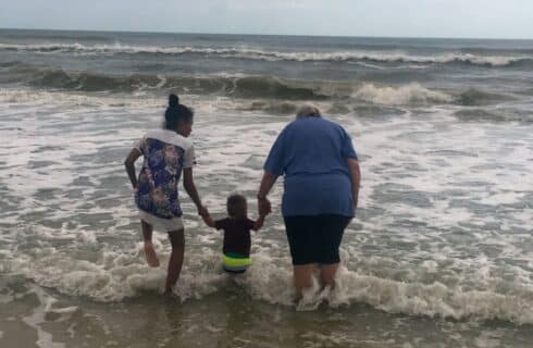 A lady and two children jumping over the waves in the ocean