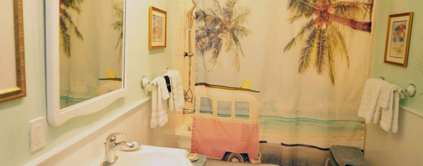 Bathroom with pedestal sink, large framed mirror and shower with curtain decorated in palm trees