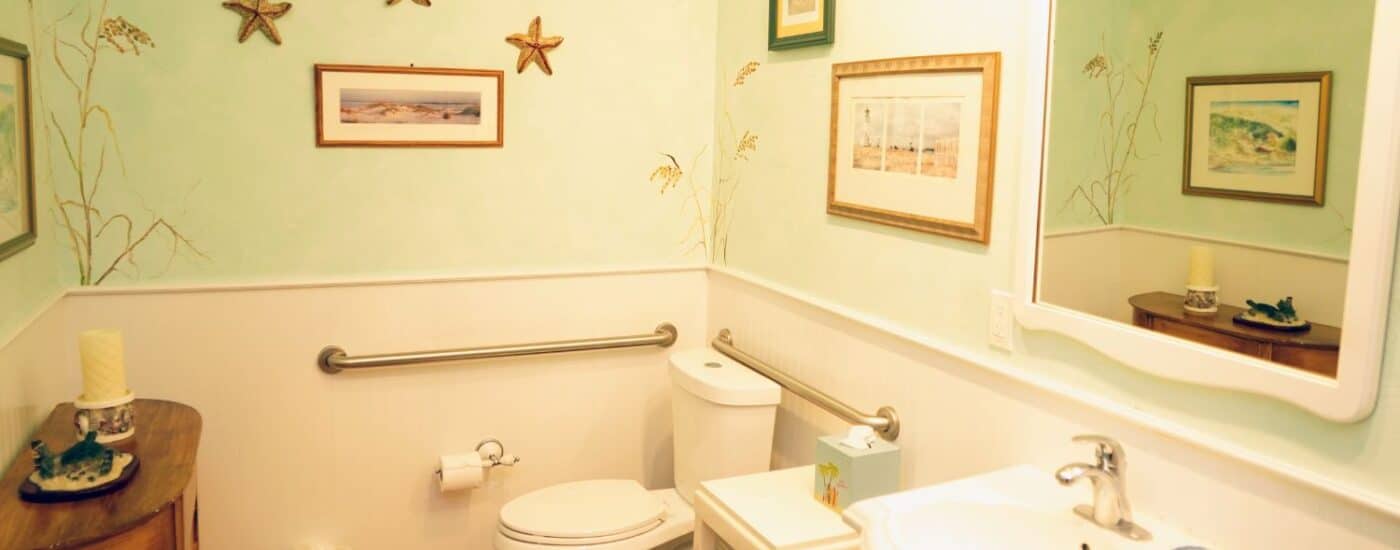 Bathroom with pedestal sink, large framed mirror, toilet, side table and decorative artwork