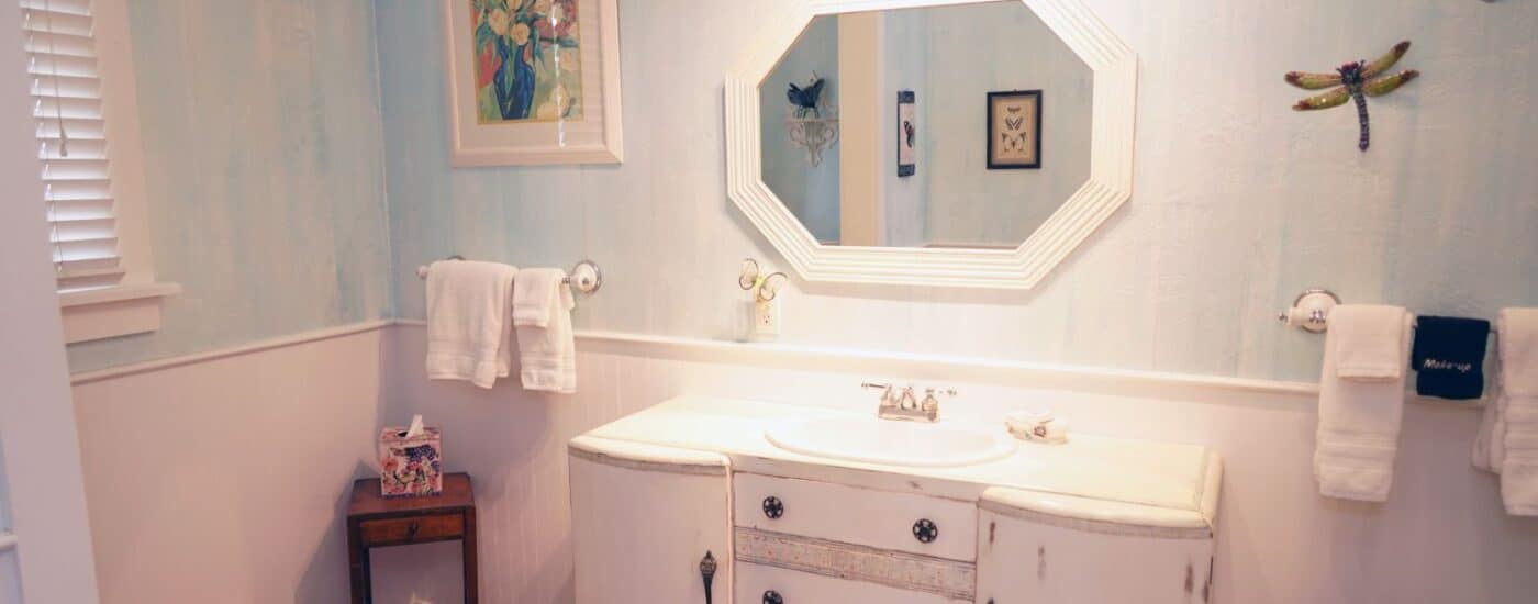 Bathroom with decorative vanity, oval mirror with white frame, plush hanging towels and window with blinds