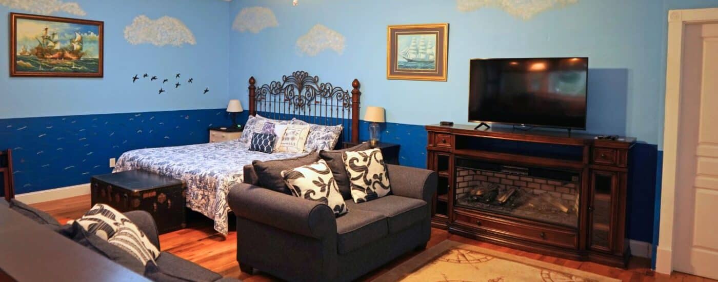 Large bedroom with king bed, gas fireplace with TV, couch and loveseat and clouds and water painted on the walls