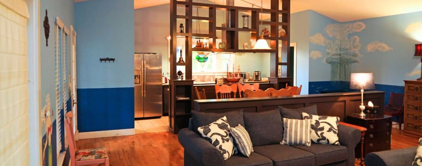 Open kitchen and living room area with stainless steel fridge, decoratively painting blue walls, couch and chair