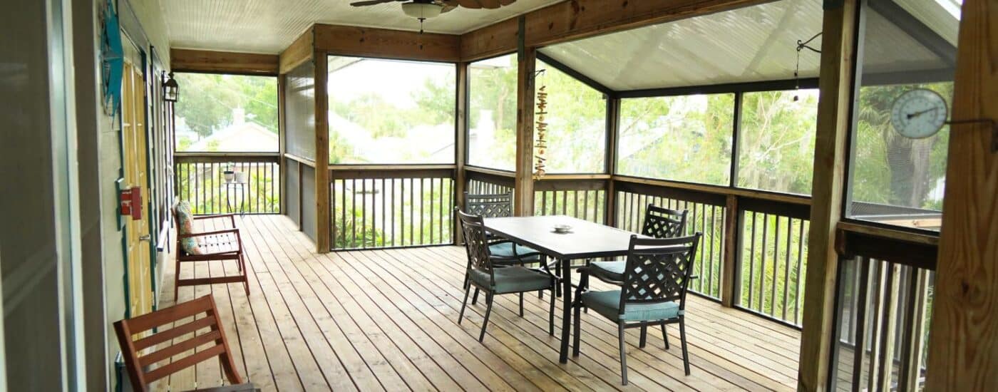 Screen in outdoor deck with table and four chairs, bench with pillow and view to green trees