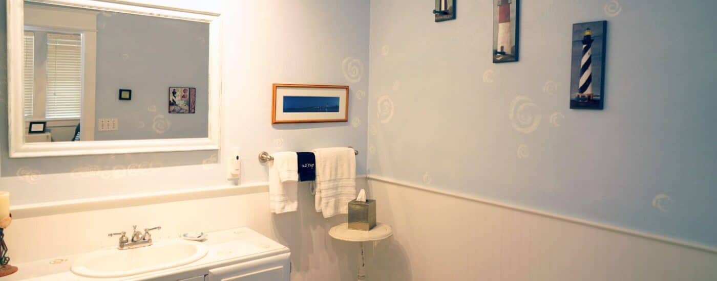 Bathroom with white vanity, large framed mirror, artwork of lighthouses