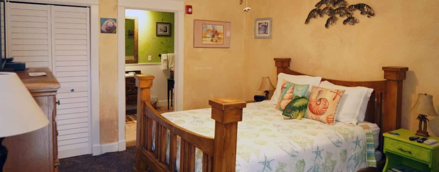 Bedroom with queen bed with seashell pattern quilt, yellow walls, manatee artwork and doorway to attached bathroom