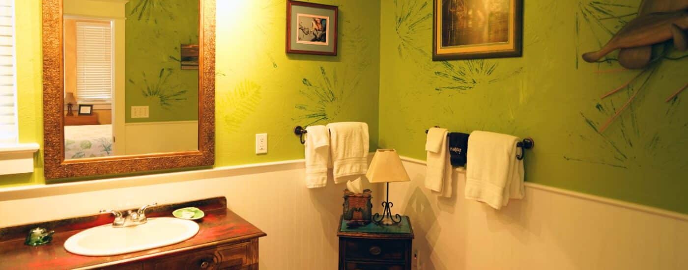 Bathroom with wood vanity, large framed mirror, decorative green walls and plush hanging towels