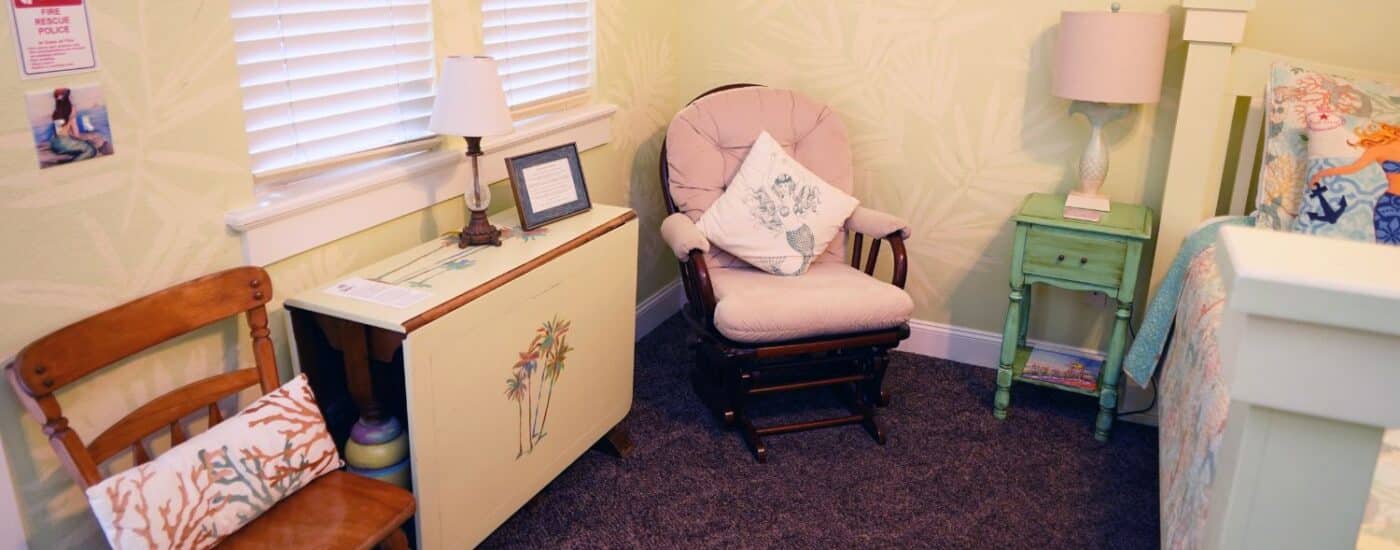 Bedroom with white bed, rocking chair, drop leaf table, windows with blinds