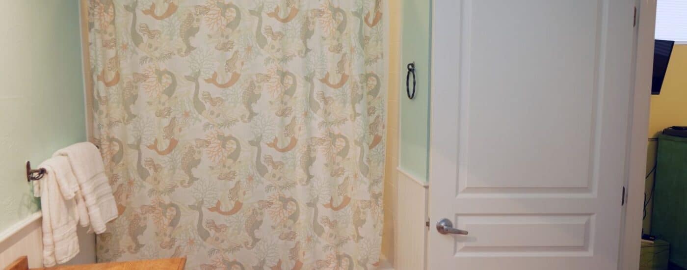 Bathroom with tub and shower, vanity with wood counter, shower curtain with mermaids