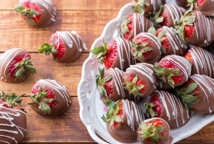 A white oval platter full of milk chocolate covered strawberries drizzled with white chocolate