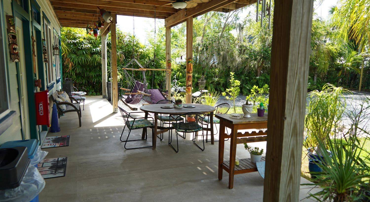 Outside back patio of a home with table and chairs, hammocks, lush green plants and palm trees